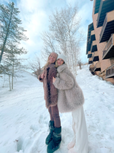 two girls hugging in après ski outfits with fur coats