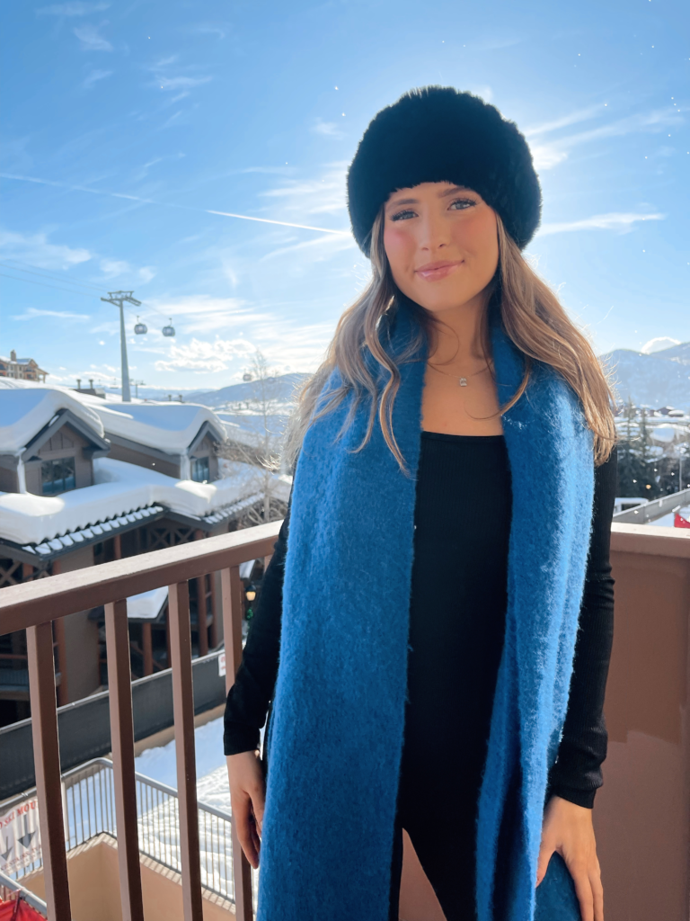 woman in an après ski outfit with a bright blue scarf and black fur headband