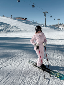 woman in a all pink ski outfit on a ski mountain with skis. used an example for a ski outfit idea for what to pack for a ski trip for beginners