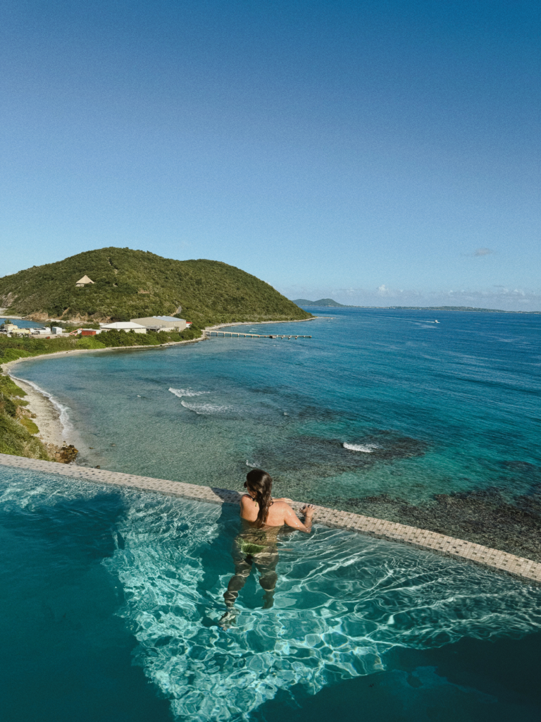 how to travel more with a full time job. image of a woman in a pool overlooking the ocean in a tropical area